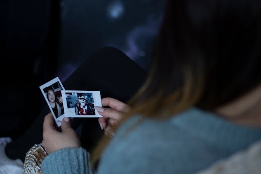 A woman sits indoors reminiscing while holding nostalgic Polaroid photos.