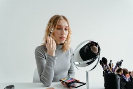 Young woman applying makeup with brush and palette in front of mirror.